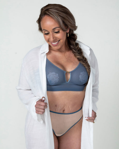 Slate / Implants & model wearing the Victoria Pocketed Keyhole bralette with gold lace trim and gold jewel that says anaono
